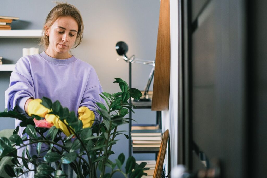 Woman wearing gloves tends to a houseplant in a cozy indoor setting.