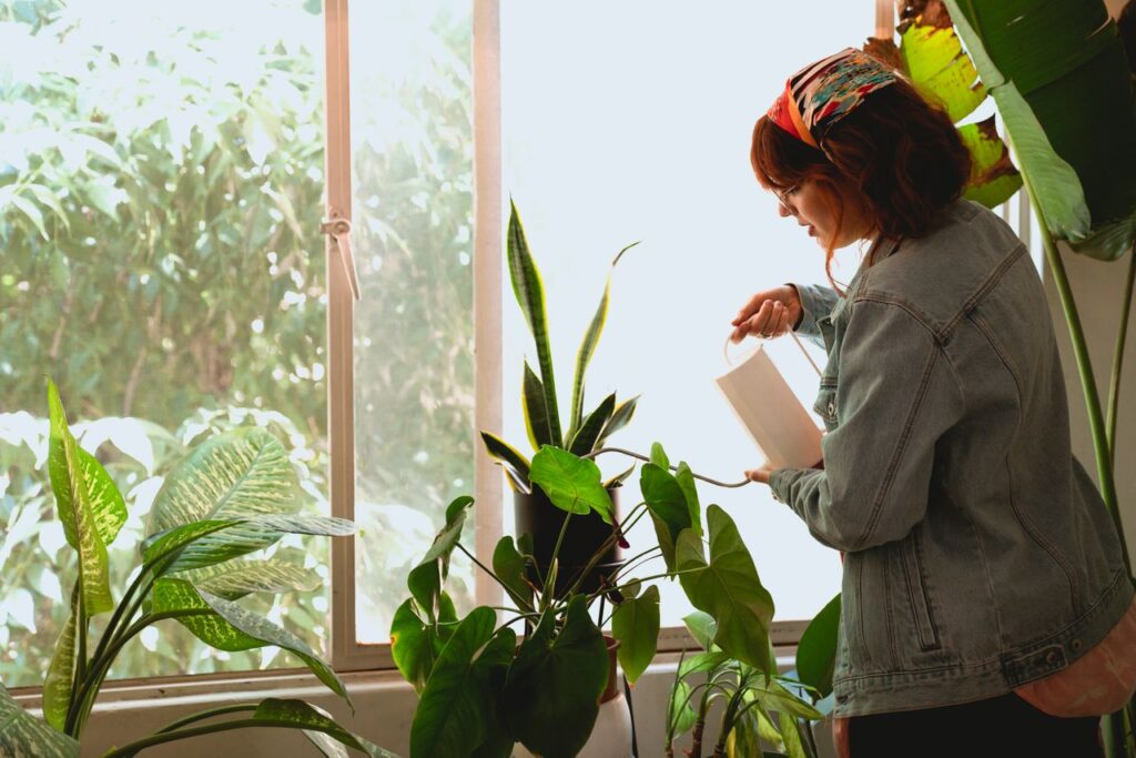 Redheaded woman nurturing green houseplants by a sunlit window indoors.