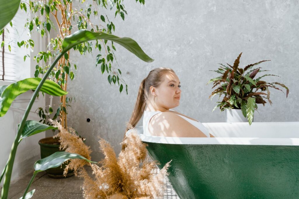 A plus-size woman enjoys a sunlit bath surrounded by lush indoor plants, embracing tranquility.