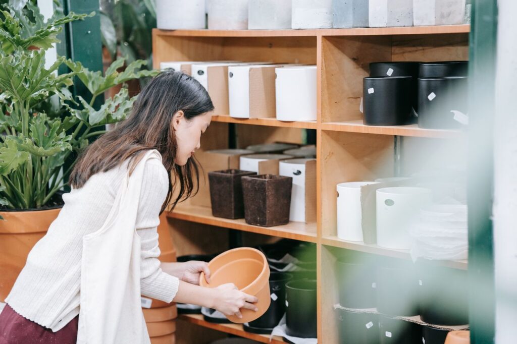 An Asian woman browses ceramic pots in an indoor garden store, selecting a terracotta pot.